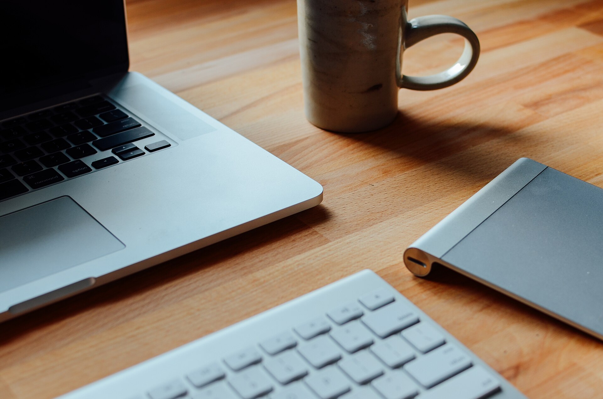 An open laptop, a mug, and a keyboard on a wooden table.